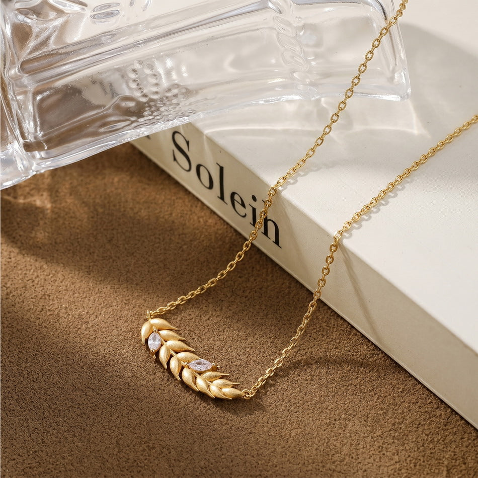 Brushed wheat ear pendant necklace styled beside a book and glass decor
